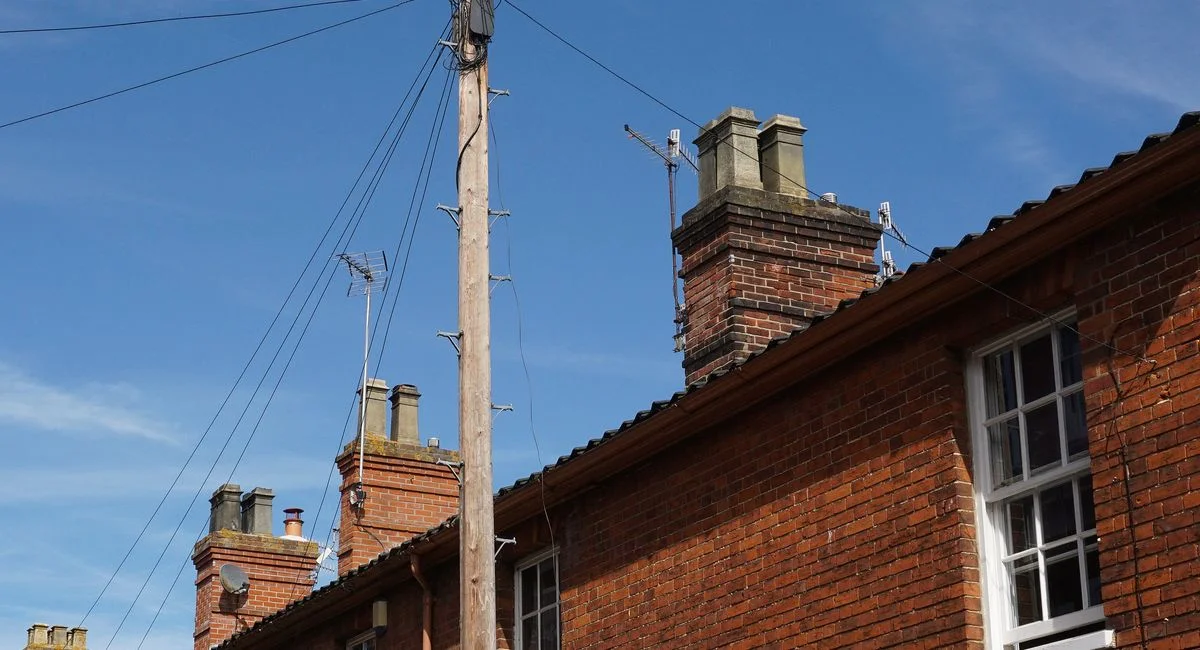A brick building featuring chimneys and an electric post under a clear blue sky.