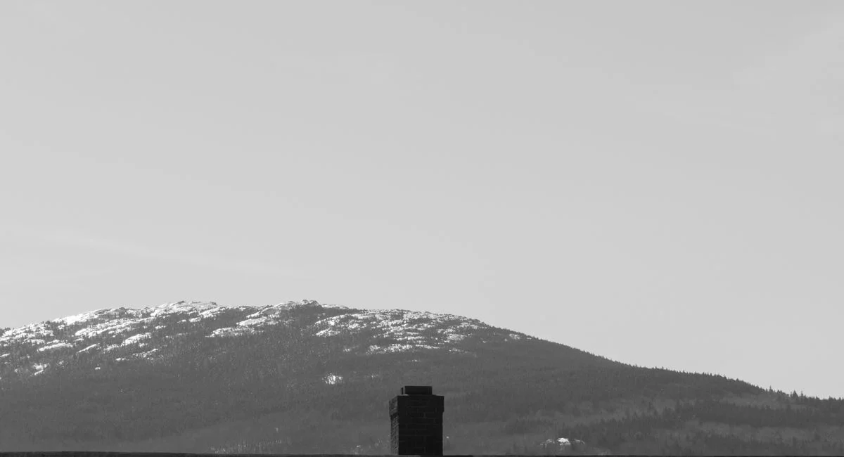 Black and white of small structure placed on road near snowy snowdrift against mountain range covered with snow in nature