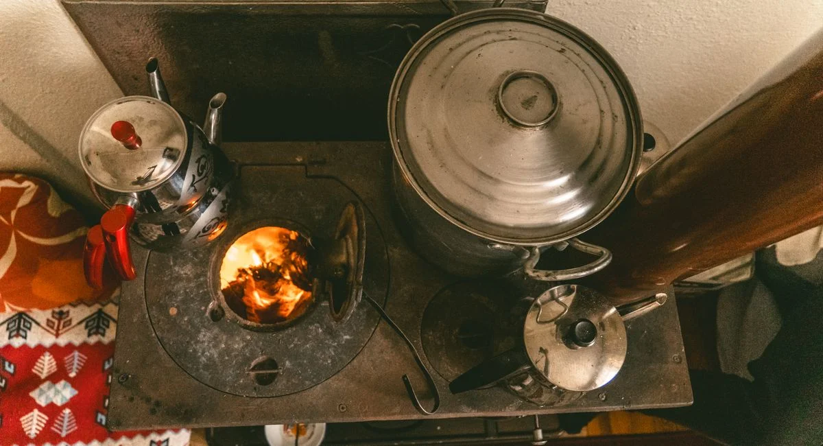 Warm rustic scene of a vintage stove with cooking pots and kettles indoors, exuding cozy vibes.