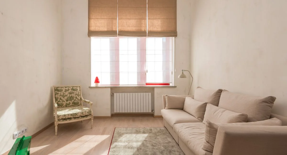 Bright, minimalist living room with beige sofa and classic armchair under warm natural light.