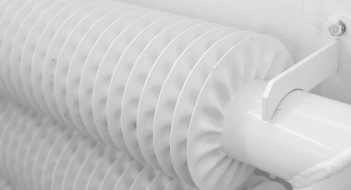 White metal tubed radiator system with pipe for industrial heating mounted to wall with hook in light room at home
