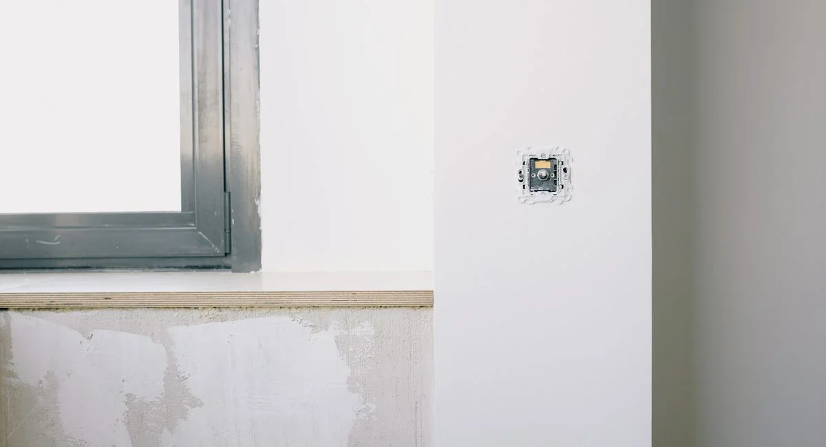 Repairs and installation of new electrical outlet on white wall near window in light apartment