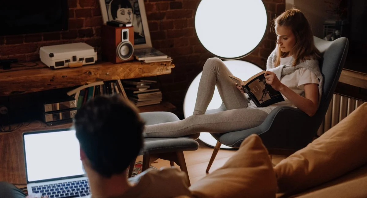Couple relaxing at home, with laptop and book, in a cozy living room.