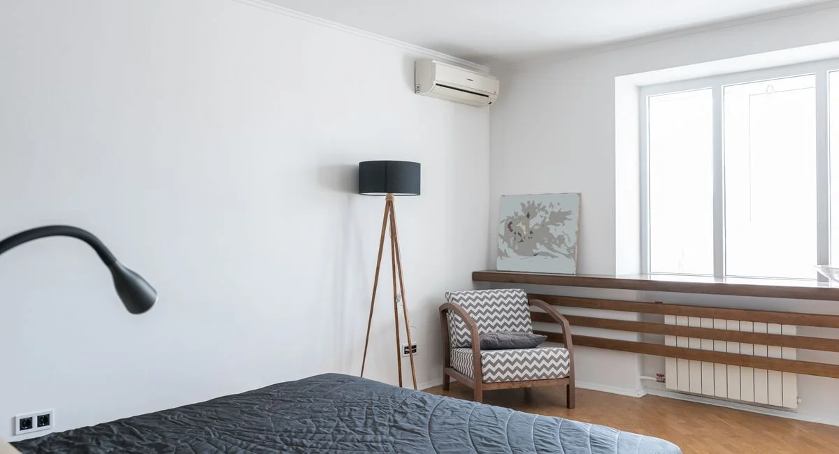 Light modern room interior with bed near lamp on floor near armchair and window near painting and air conditioner