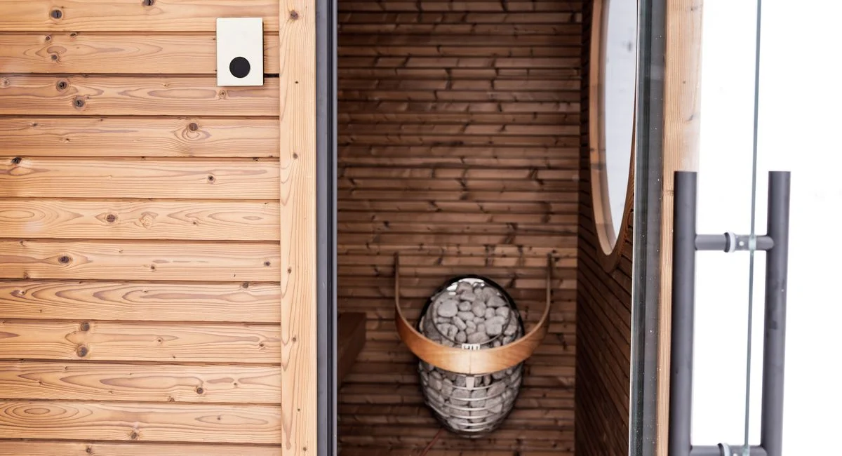 A stylish wooden sauna featuring a modern design with an electric heater and stones, perfect for relaxation.