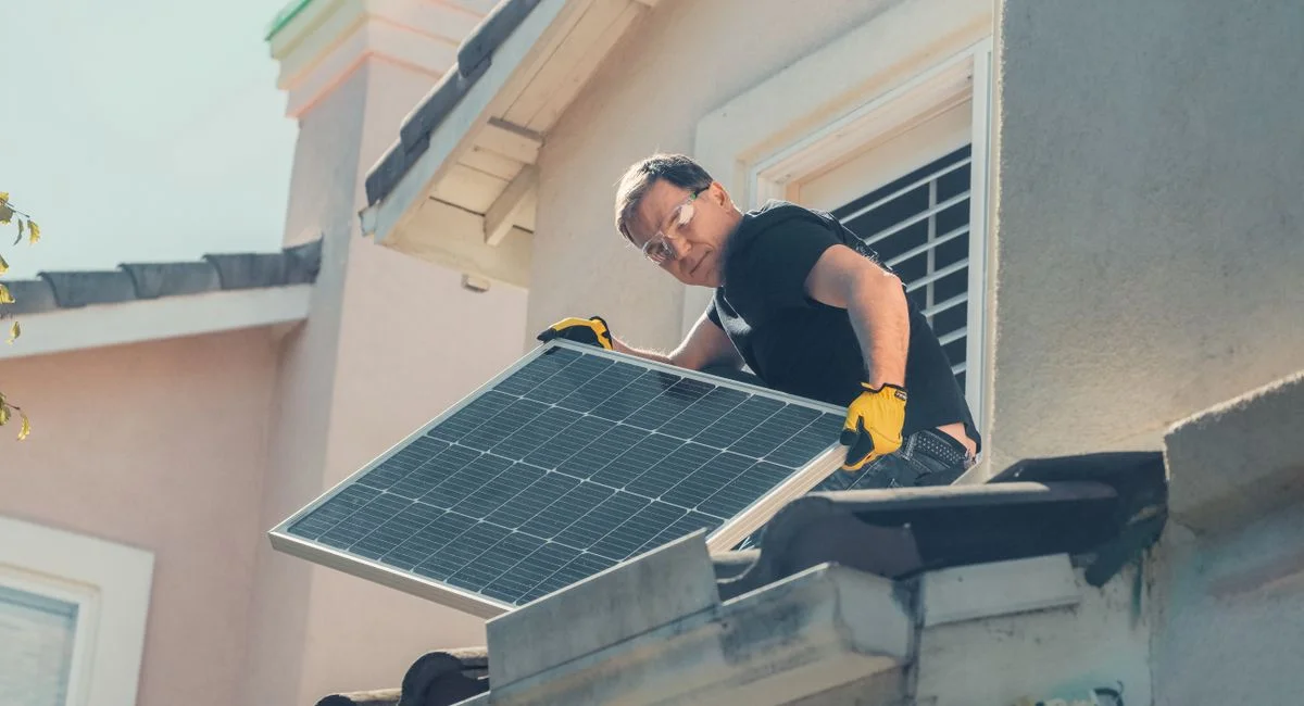 A technician in protective gear installs solar panels on a house roof, promoting sustainability.
