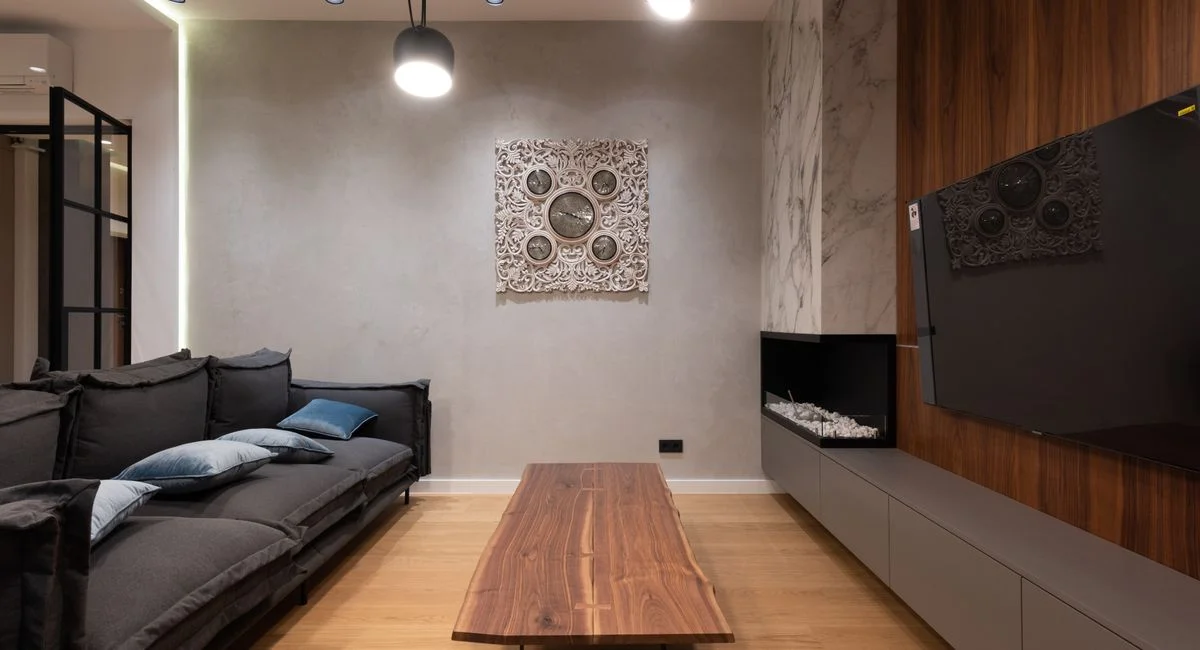 Soft couch with cushions placed against wooden coffee table and modern TV set hanging on wooden wall near fireplace in spacio