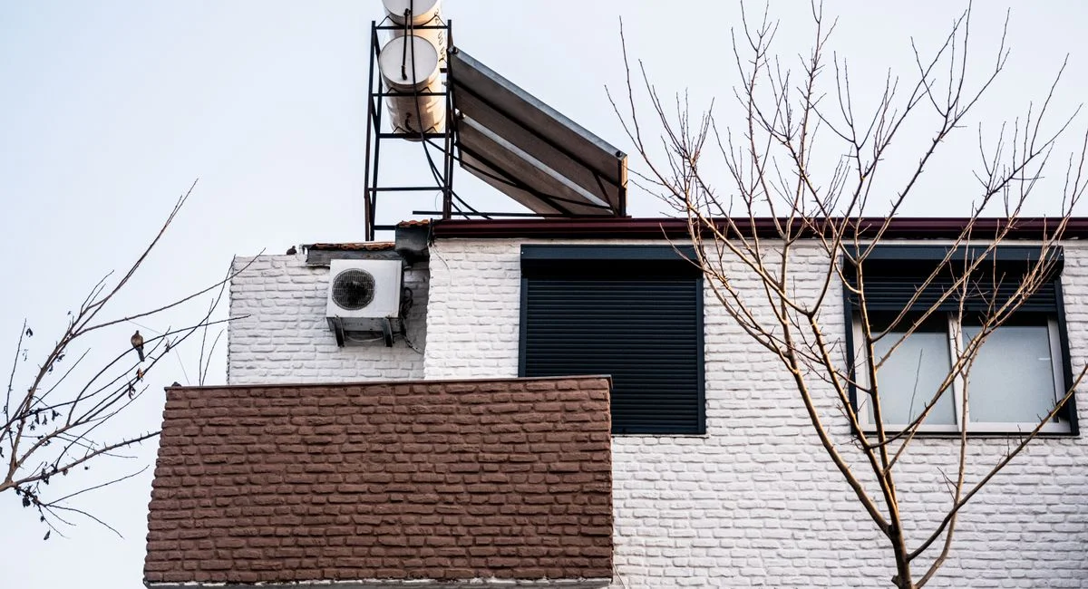 A minimalist building facade with air conditioner and bare winter trees, viewed from a low angle.