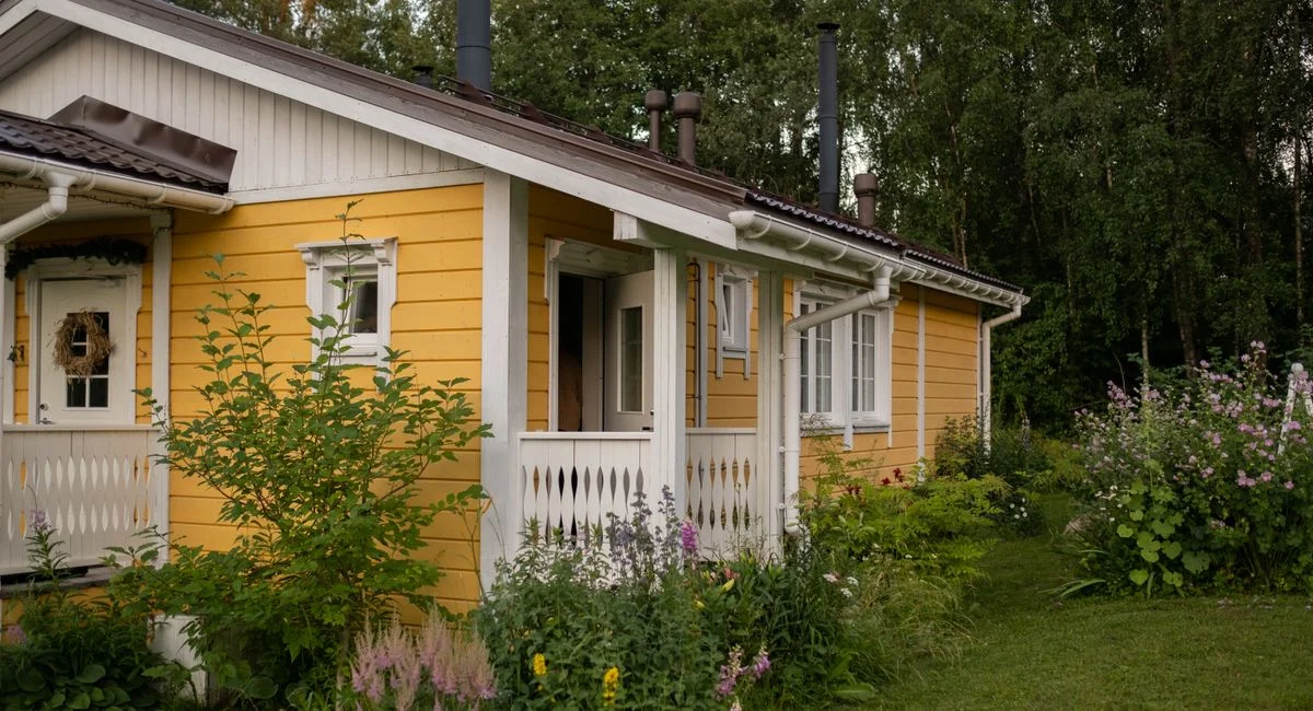 A picturesque yellow cottage surrounded by lush greenery and summer blooms in a peaceful rural area.