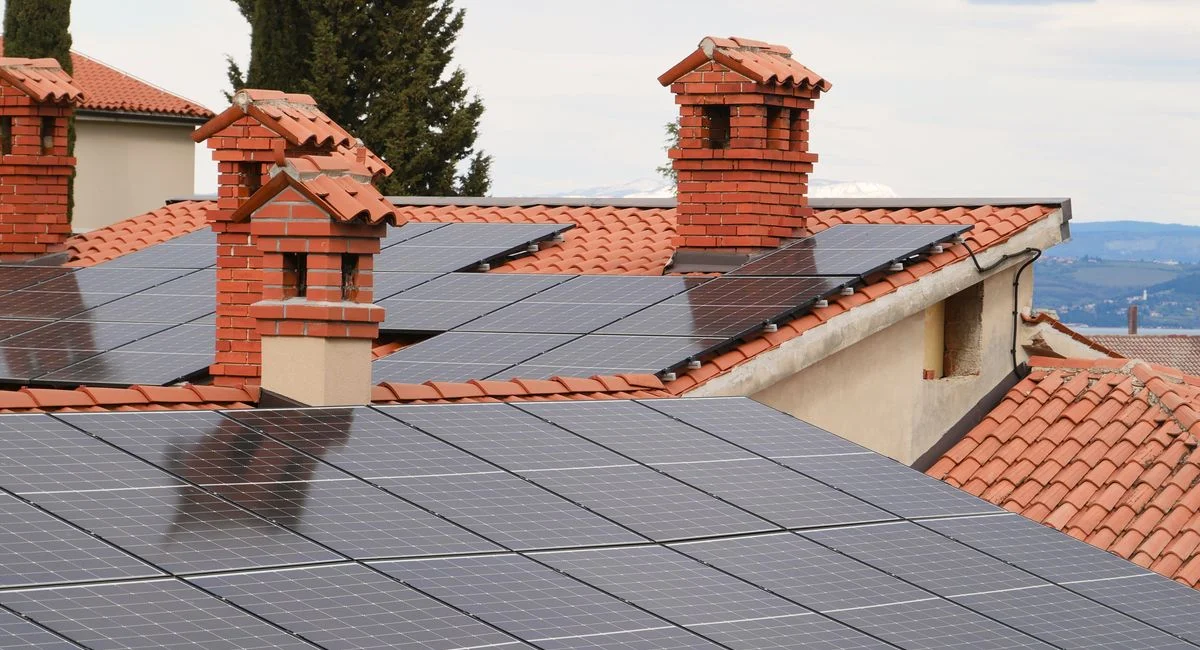 Solar panels on tiled roofs of houses with chimneys, capturing clean energy.