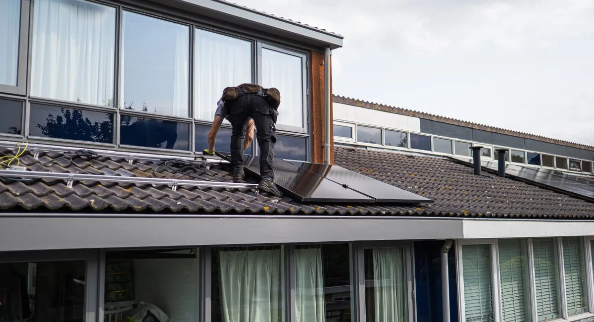 Technician working on installing solar panels on a residential rooftop during the day.