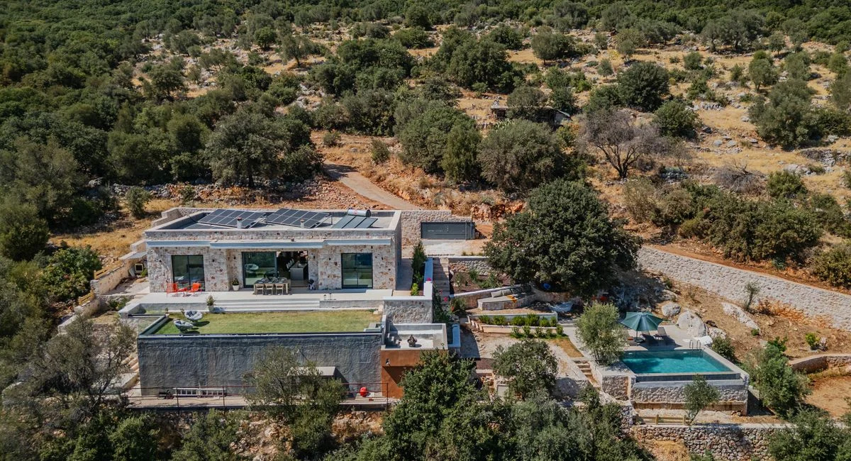 Aerial view of a modern luxury villa with a pool set in a scenic countryside landscape.