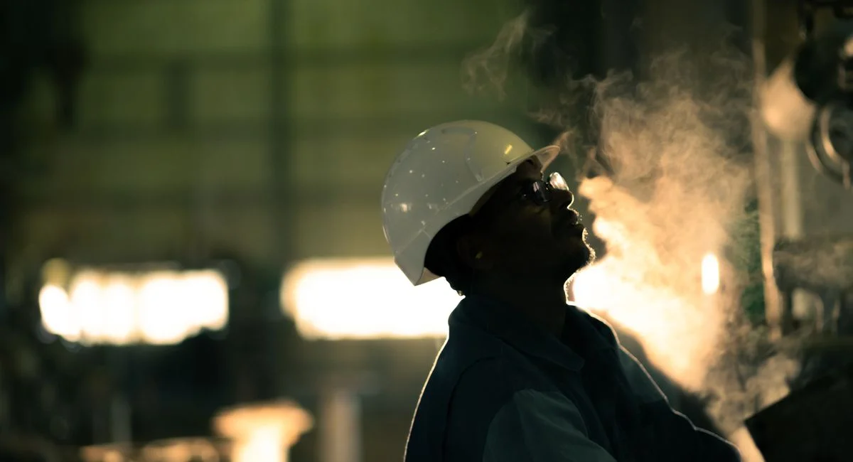 A worker in hard hat surrounded by steam in an industrial setting, conveying energy industry.