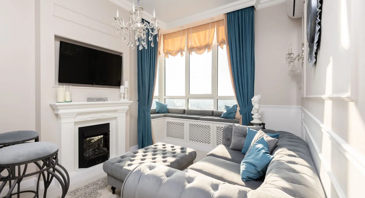 Contemporary living room interior with couch and fabric bench under chandelier against television with black screen in sunlig