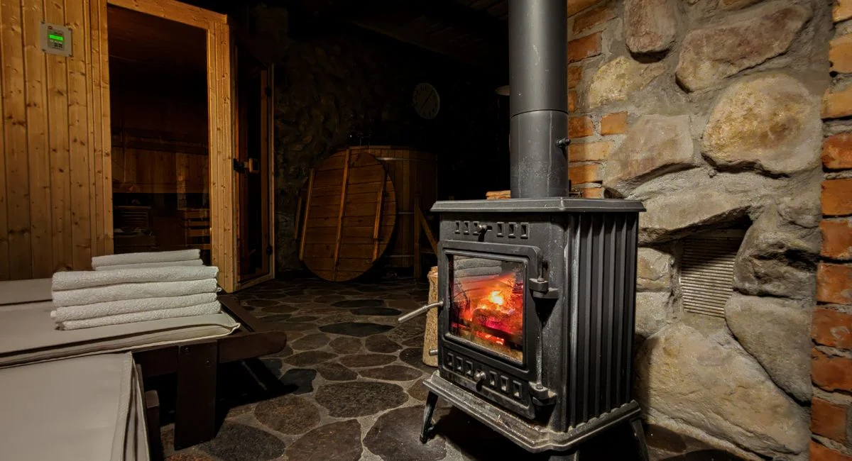 Warm sauna room in Płociczno featuring a classic wood-burning stove and rustic stone walls.