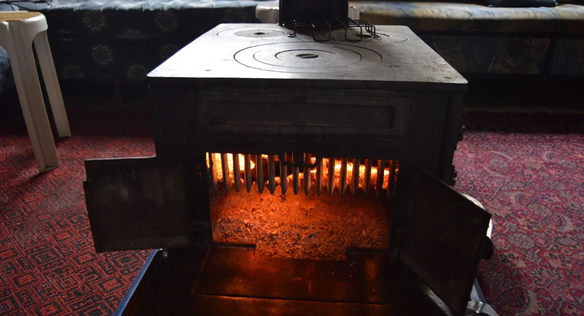 A classic vintage wood heater radiating warmth in a cozy, carpeted interior room.