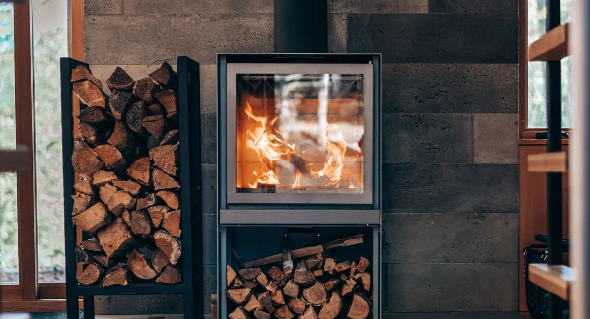 Contemporary square fireplace with burning flame and fuel woods stand located in stylish modern cottage