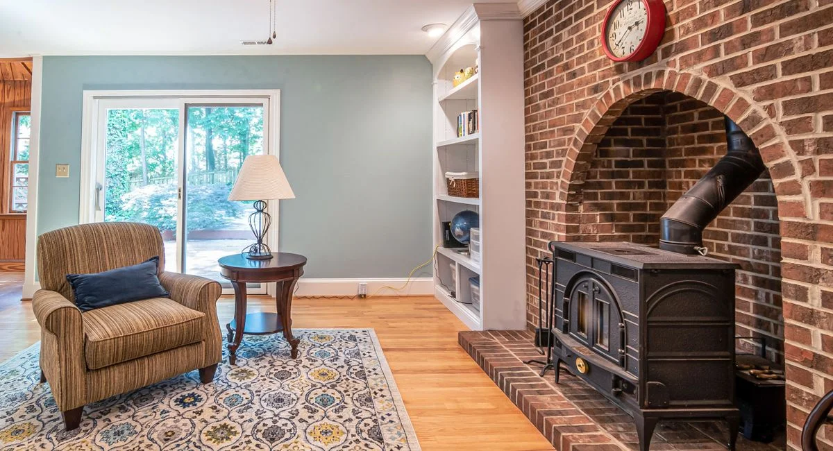 Charming living room with a fireplace, armchair, and window view for a homey atmosphere.