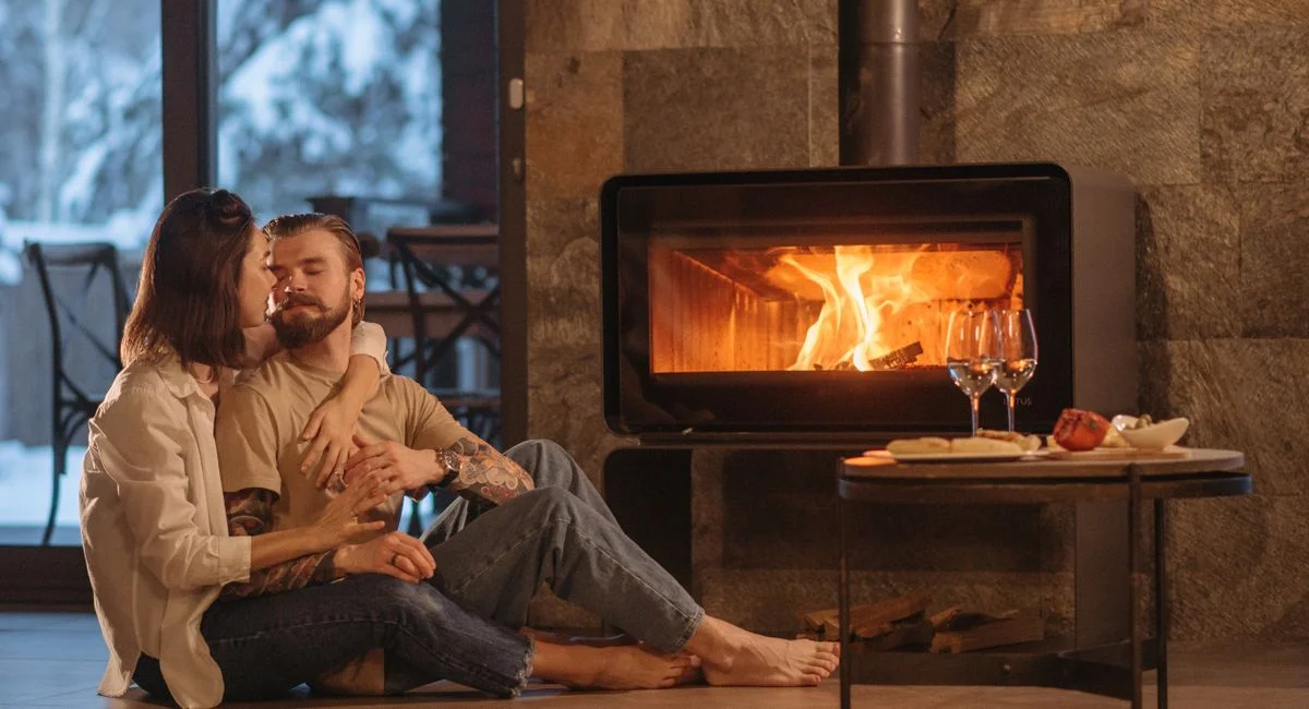 A couple enjoys a warm embrace by the fireplace inside a cozy home during winter.