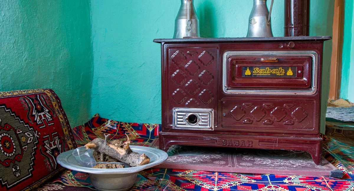 Traditional rustic stove with wood in a vibrant, cozy room with patterned textiles.
