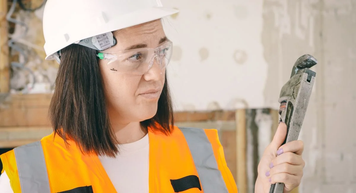 Caucasian woman in PPE holding a plumber's wrench indoors, focused on maintenance.