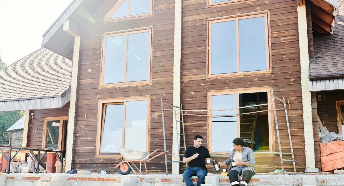 Two individuals enjoying coffee during a break at a wooden house construction site.