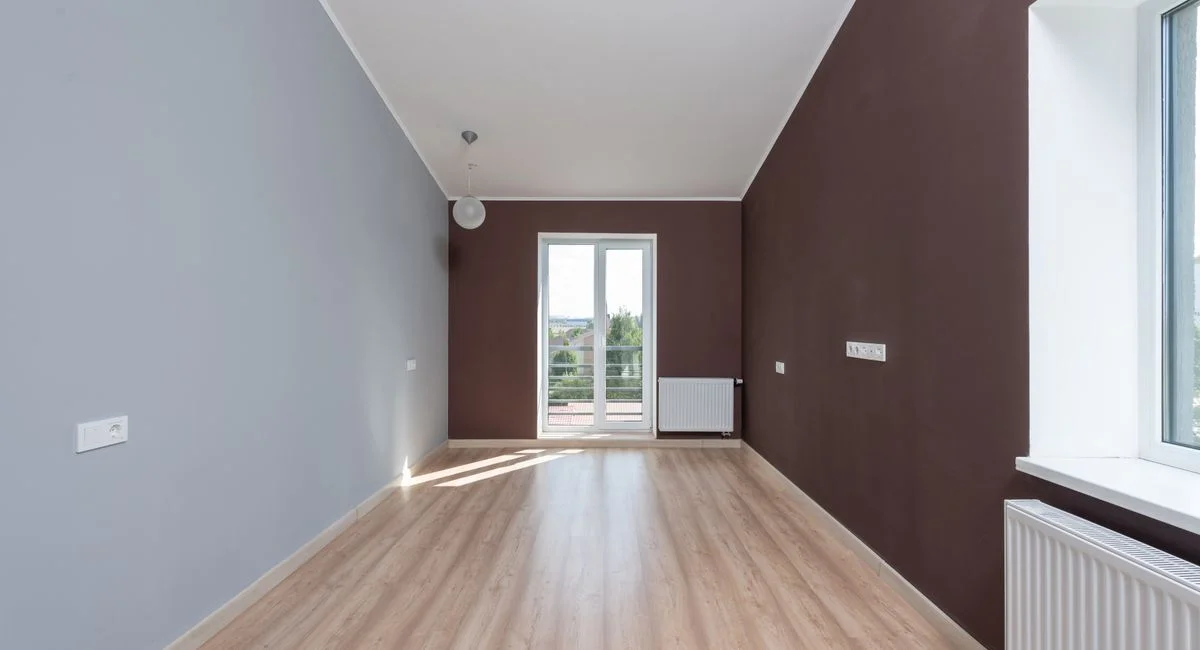 Spacious empty room featuring wooden flooring and a large window with natural light.