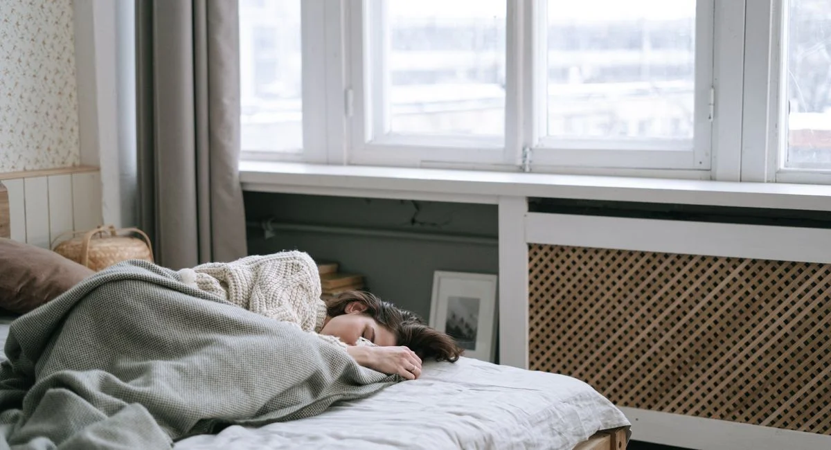 Woman peacefully sleeping in a cozy bedroom with soft light and warm blankets.