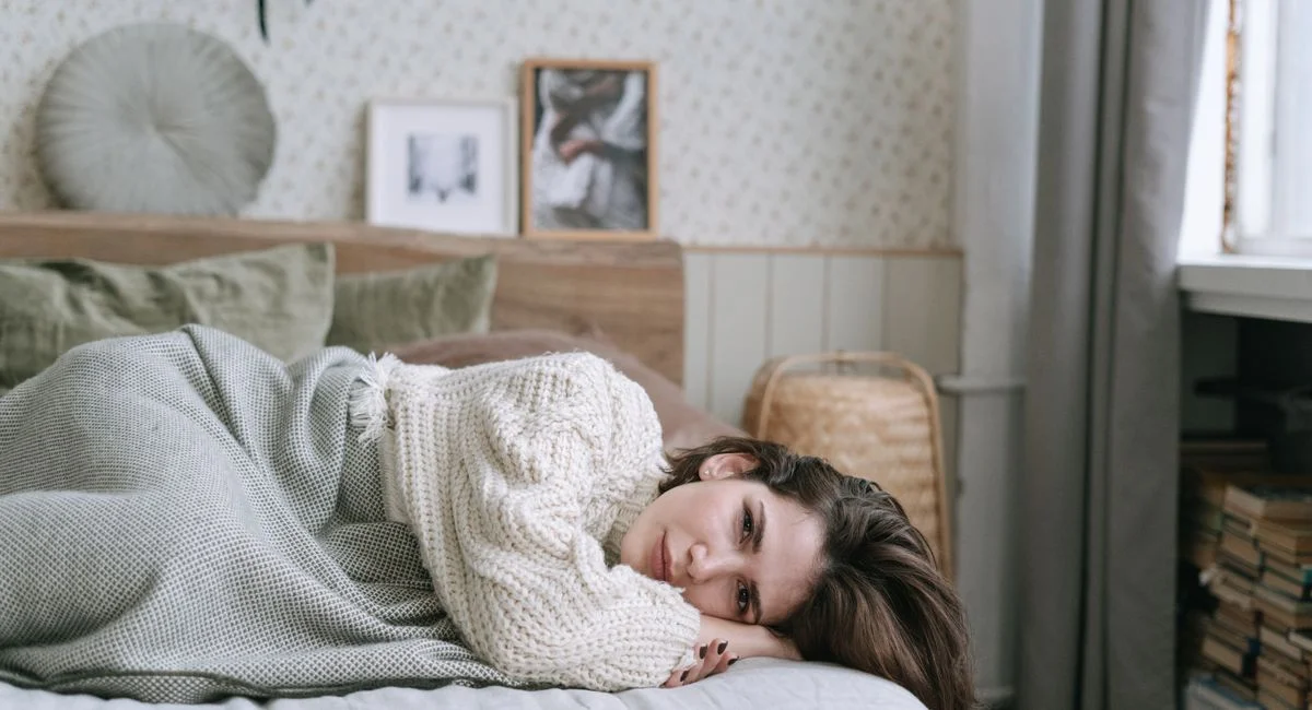 A woman in a knitted sweater lies on a bed, creating a cozy atmosphere.
