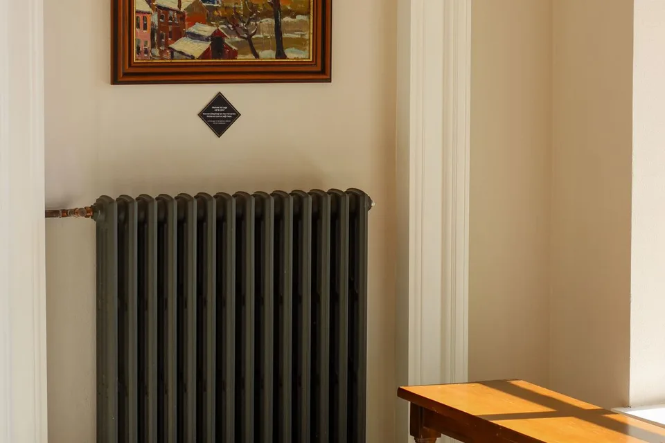 Radiateur en fonte sous un tableau dans une pièce éclairée par le soleil